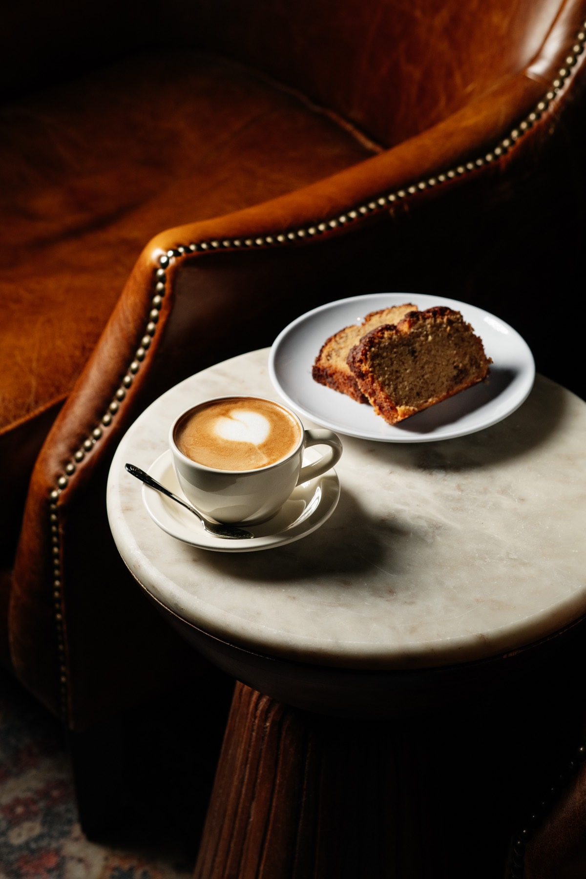 A cappuccino and a slice of cake beside a leather armchair at It's Him