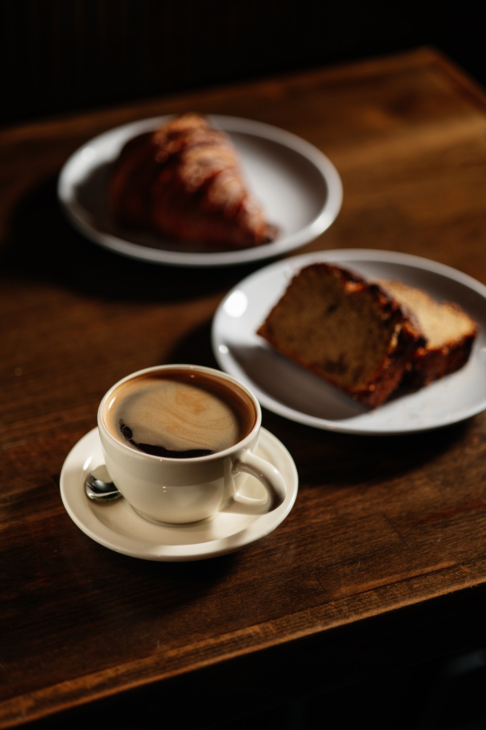 A cappuccino, a croissant, and a slice of cake on a wooden table