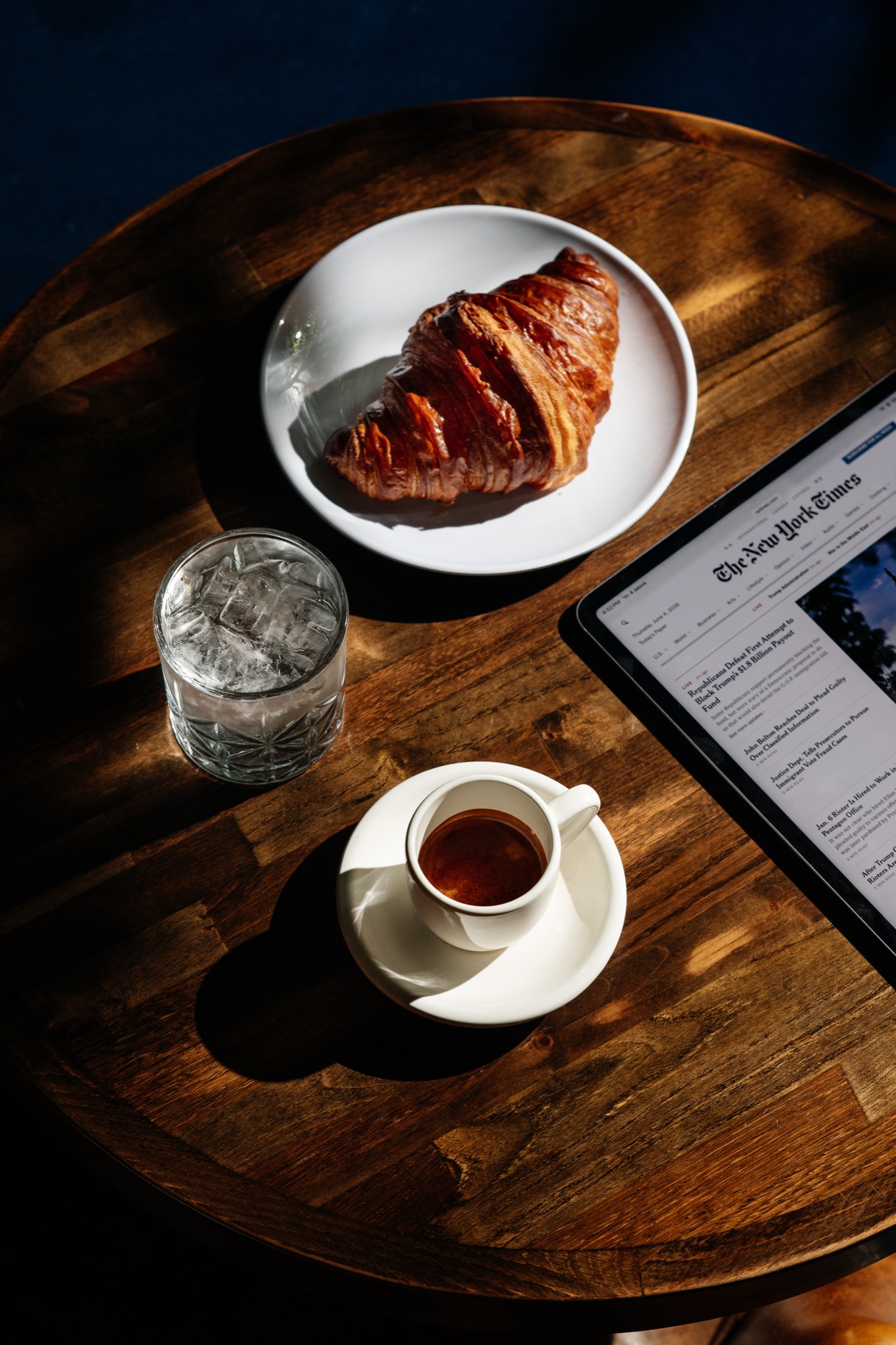 Morning light on a wooden table — espresso, a croissant, and the day's news on a tablet at It's Him